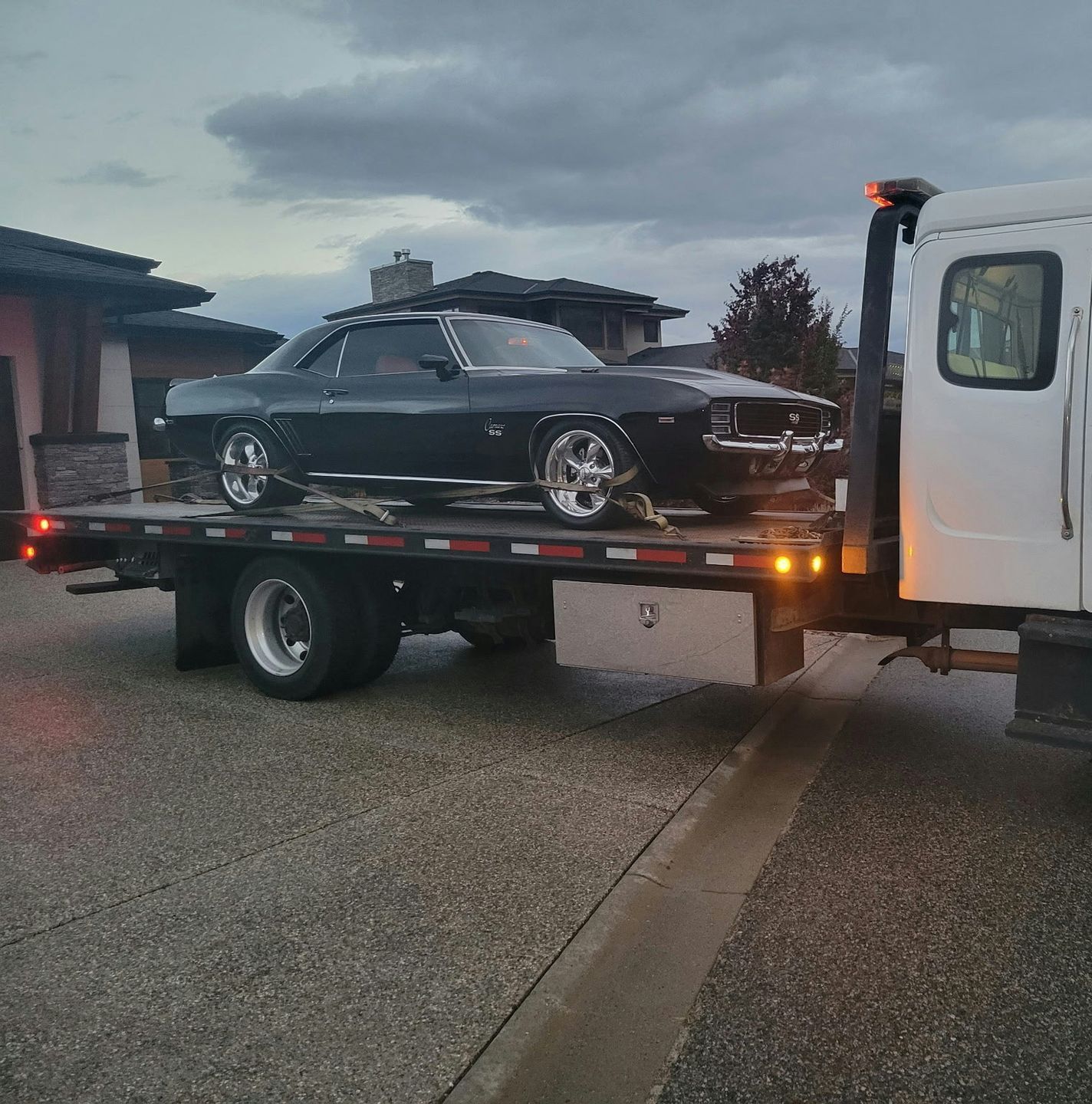 A black classic car loaded onto a tow truck.